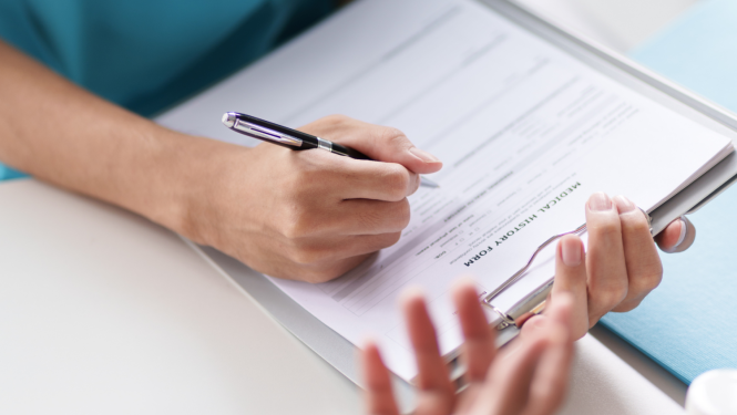 Close-up of a person filling out a medical history form on a clipboard