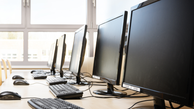 Datoru klase ar melnu monitoru, tastatūru un peļu rindu uz galda pretī logiem