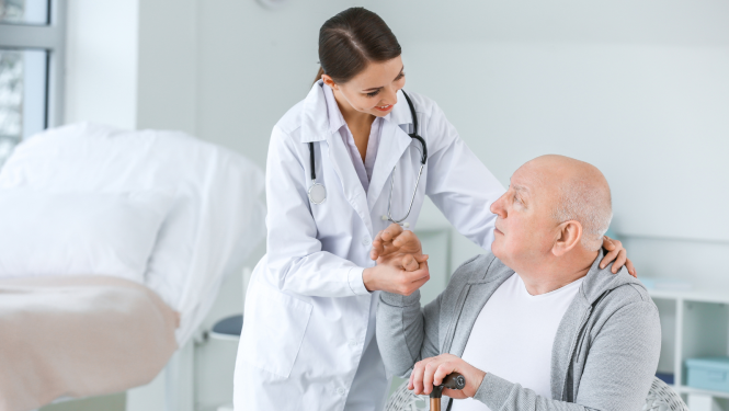 medicīnas darbiniece vai ārste sniedz atbalstu gados vecākam vīrietim ar spieķi gaišā palātā.