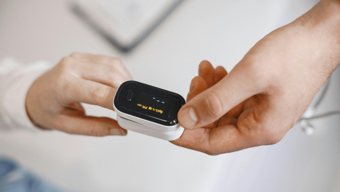 Pulsa oksimetrs uz pirksta, ko tur medicīnas darbinieks.