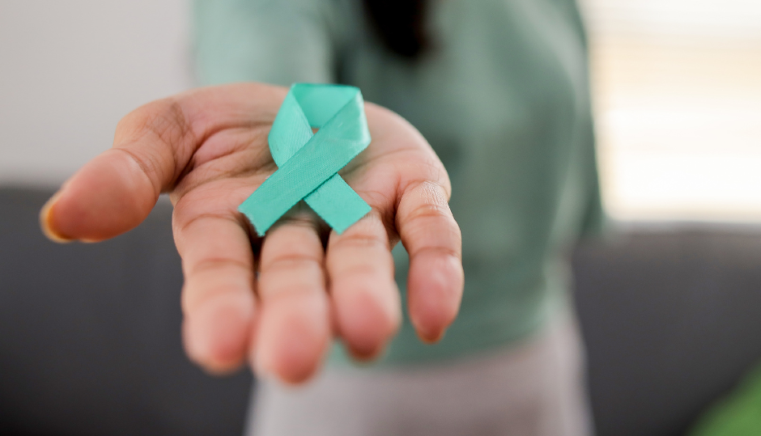 Sievietes plaukstā redzama tirkīzzila atbalsta lentīte, kas simbolizē dzemdes kakla vēža profilaksi un skrīningu