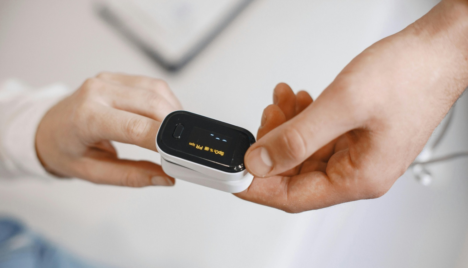 Pulsa oksimetrs uz pirksta, ko tur medicīnas darbinieks.